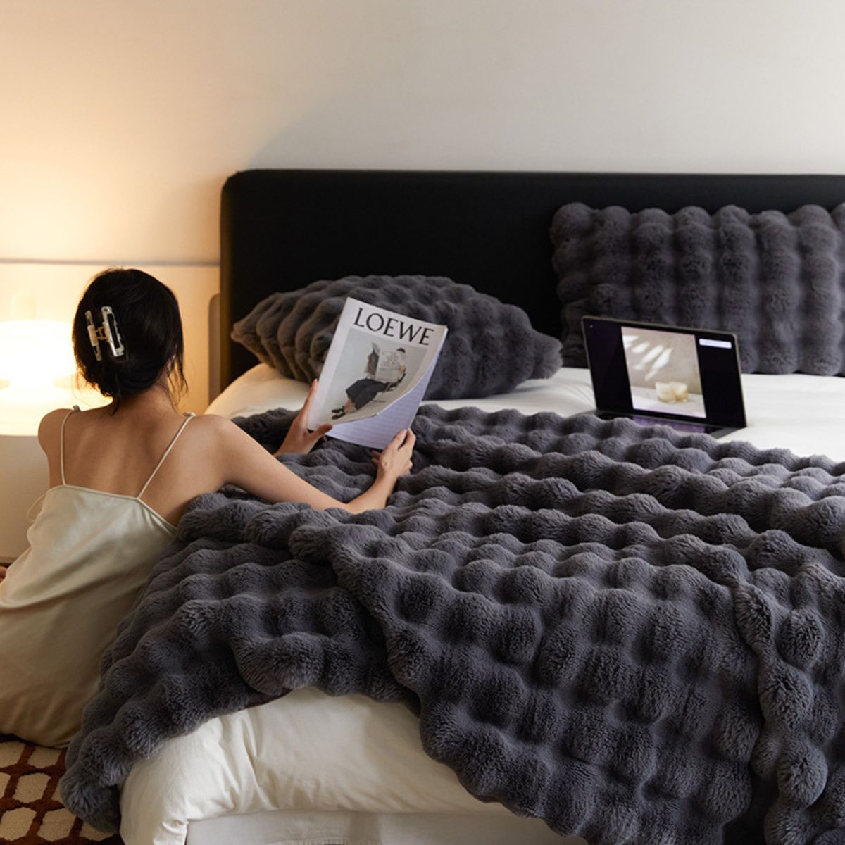 Charcoal grey bubble texture fleece blanket on bed, lifestyle scene with woman reading
