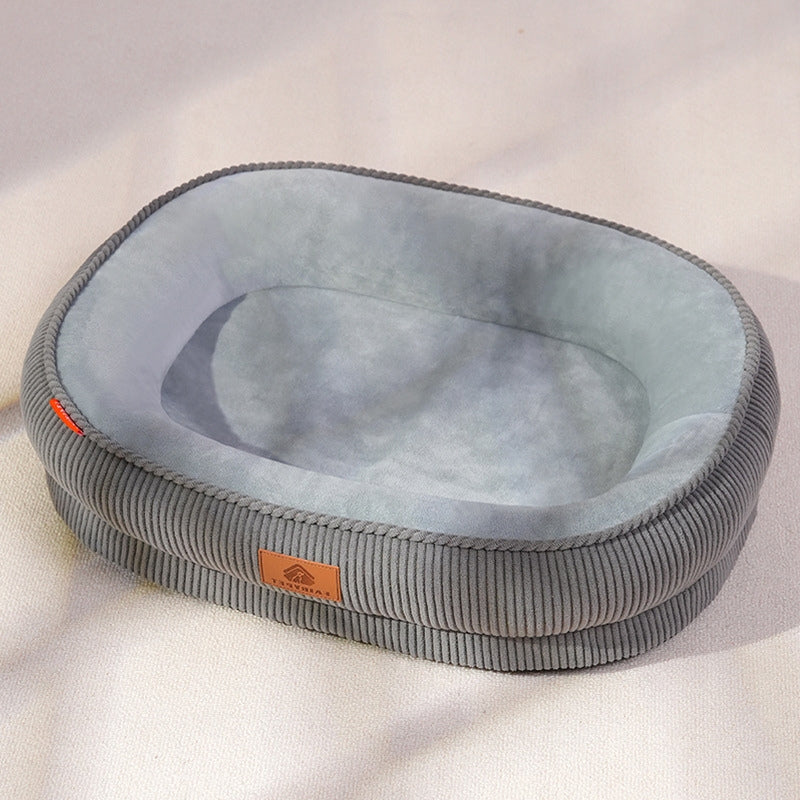 A cozy gray oval pet bed with a corduroy texture, placed on a light-colored floor, showing its modern design in a natural home environment.
