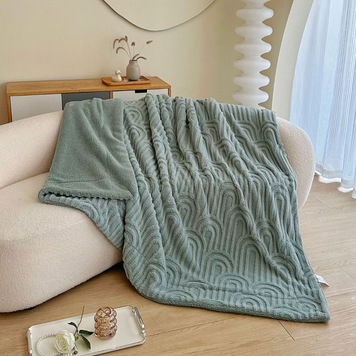 Sage green fleece throw blanket draped on cream sofa in natural light