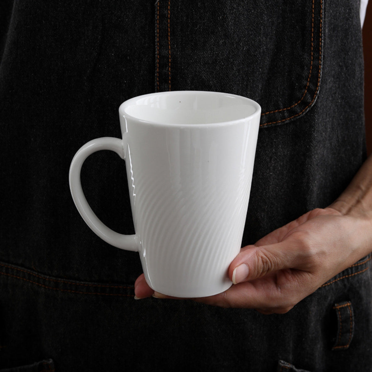 CAI tall white ceramic coffee mug held in hand, textured surface close-up.