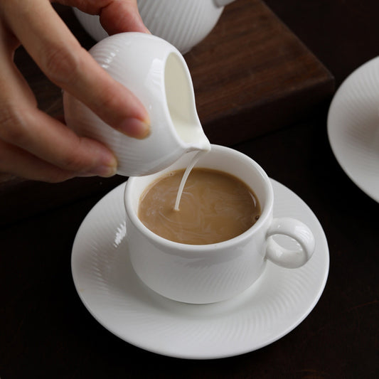 CAI milk pitcher pouring cream into coffee cup on saucer, lifestyle shot.