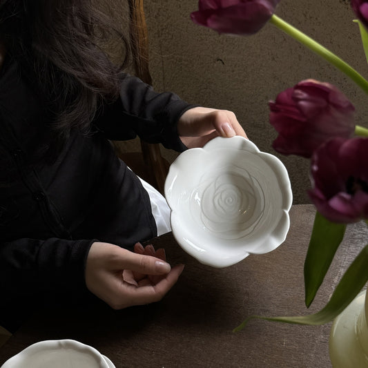 Person holding small ceramic bowl shaped like rose petals in natural light.