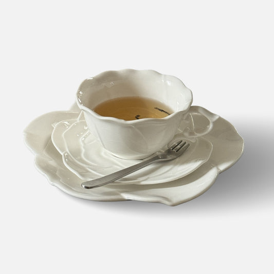 White ceramic tea cup and rose-shaped plate set with tea and dessert fork.
