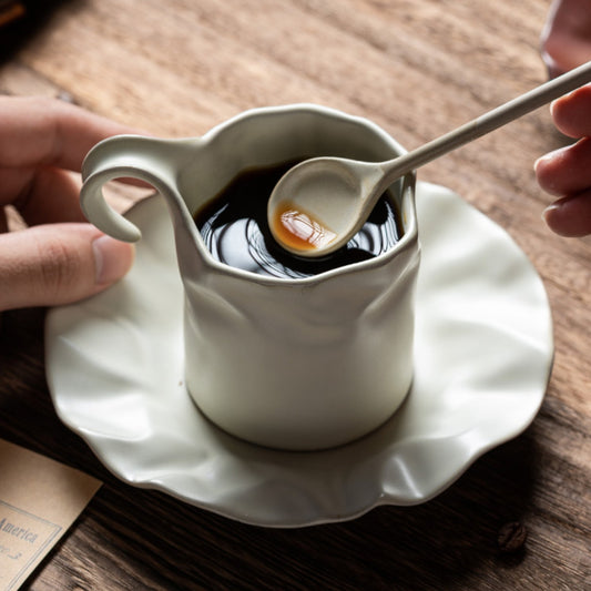Artistic ceramic coffee cup with matching saucer and spoon on rustic wooden table.