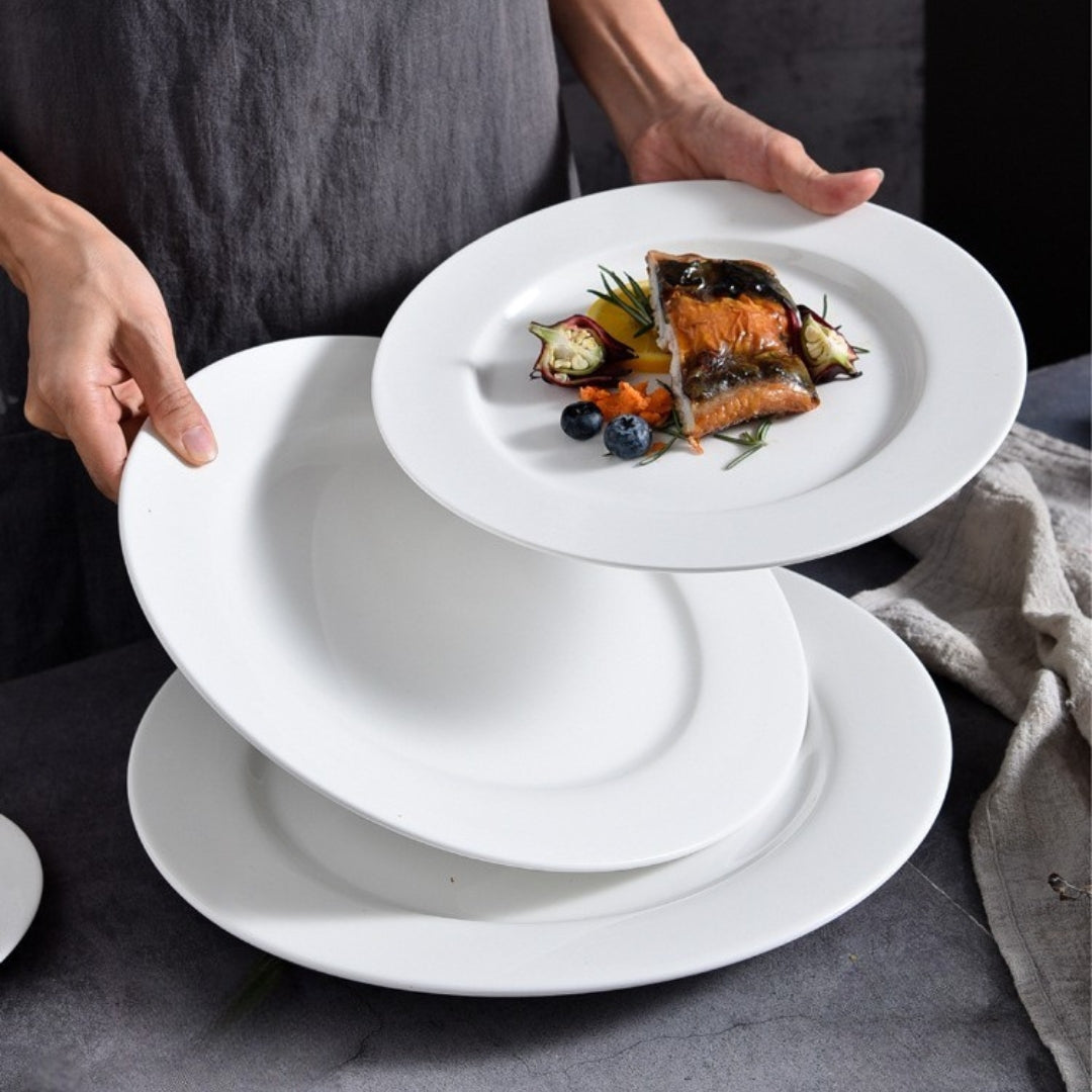 Person holding and stacking white ceramic plates with plated fish dish