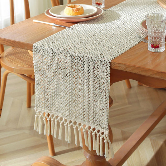 Beige lace crochet-style woven table runner with tassel fringe on wooden table