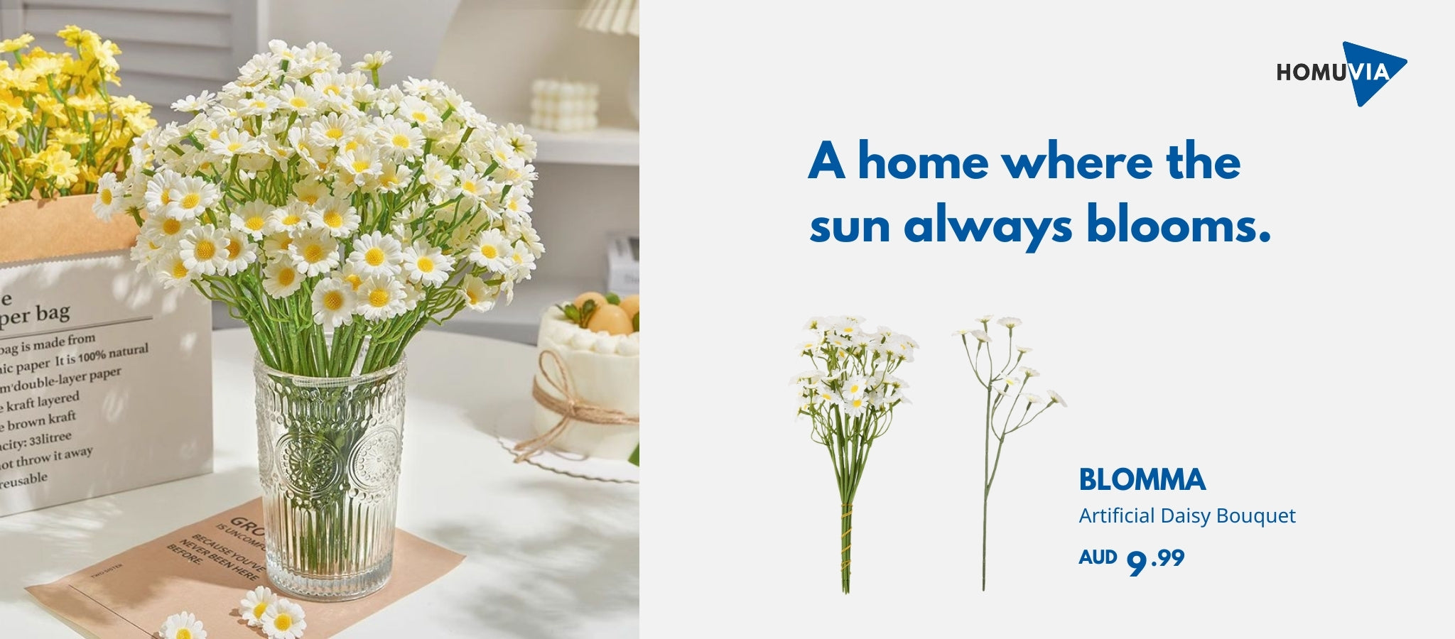 A delicate bouquet of white faux daisies with yellow centers, arranged in a vintage-style textured glass vase. The vase sits on a bright tabletop next to a brown paper bag and a slice of cake, capturing a cheerful and minimalist home decor scene.