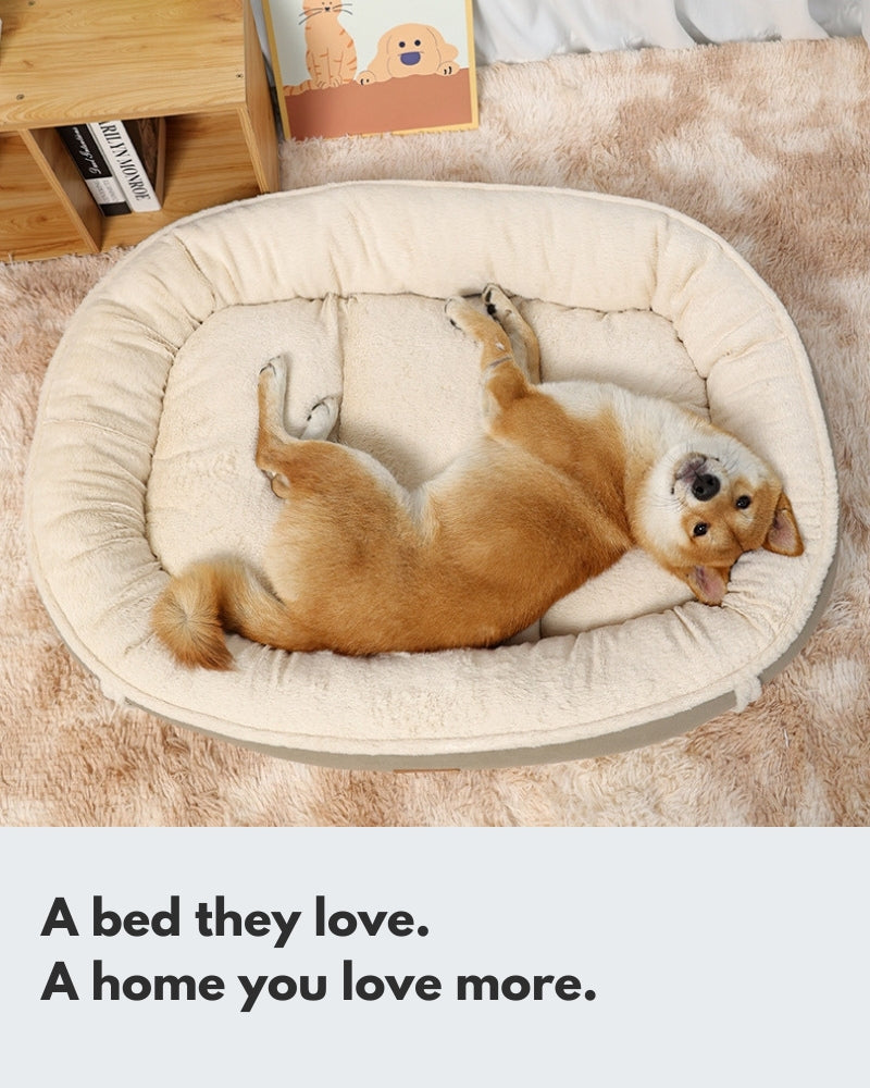 A happy golden Shiba Inu lies on its back in a fluffy, beige pet bed, with its paws in the air and a joyful smile directed at the camera. The plush dog bed looks comfortable and warm, blending seamlessly with the surrounding cozy home environment.