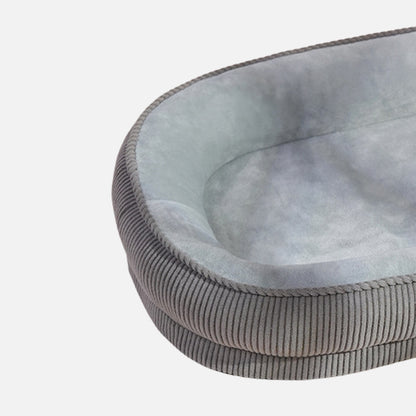 A close-up side view of a gray oval pet bed, highlighting the ribbed corduroy fabric on the outside and the soft plush material on the inside.