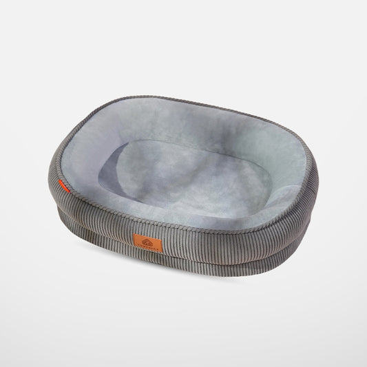 A full product shot of a gray oval pet bed with a ribbed corduroy exterior and a plush light gray interior, isolated against a white background.