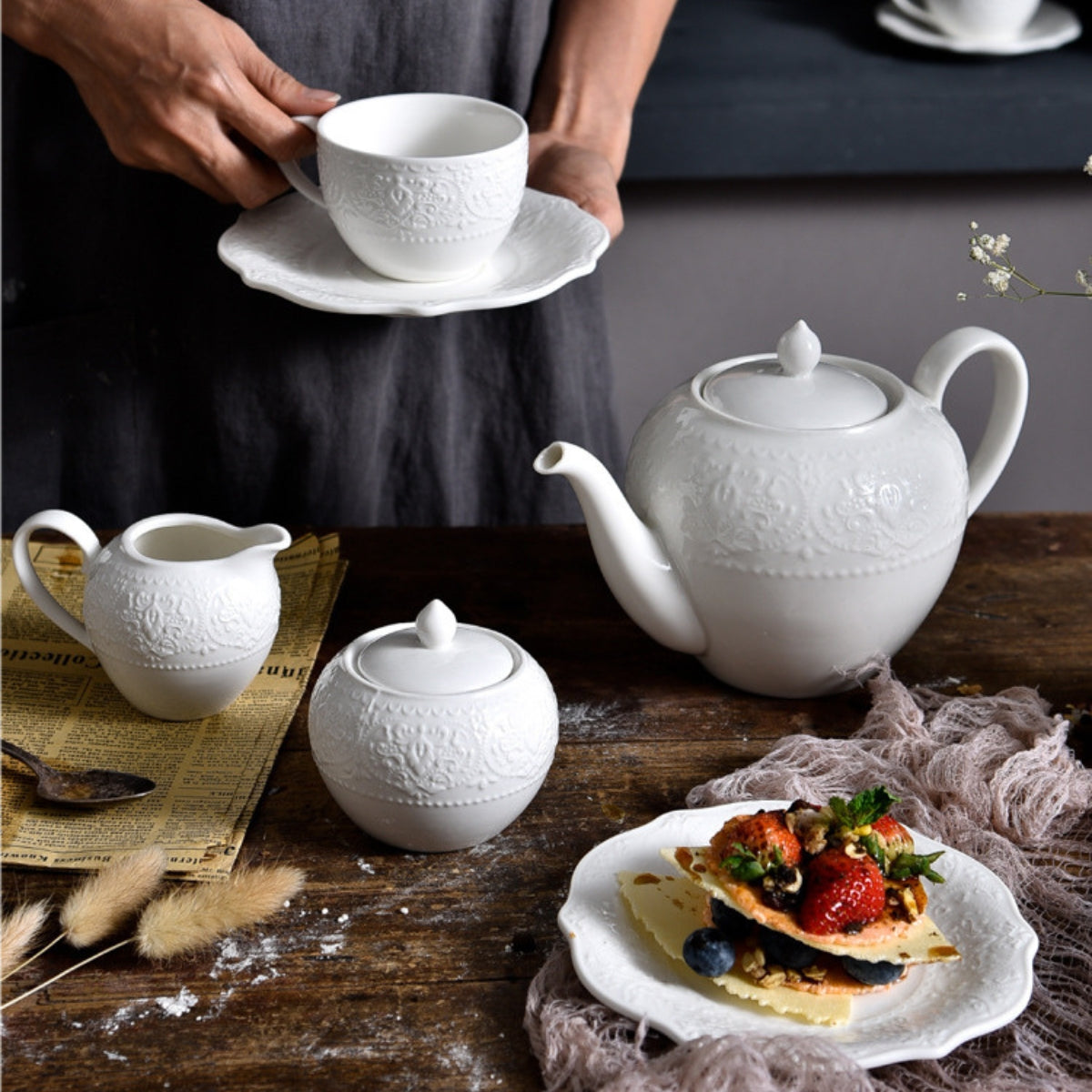 JUN HUA embossed ceramic tea set on rustic table with dessert and cup in hand.