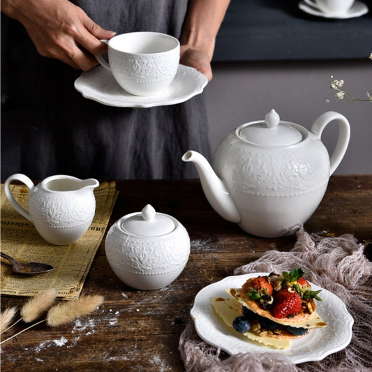 JUN HUA embossed ceramic tea set on rustic table with dessert and cup in hand.
