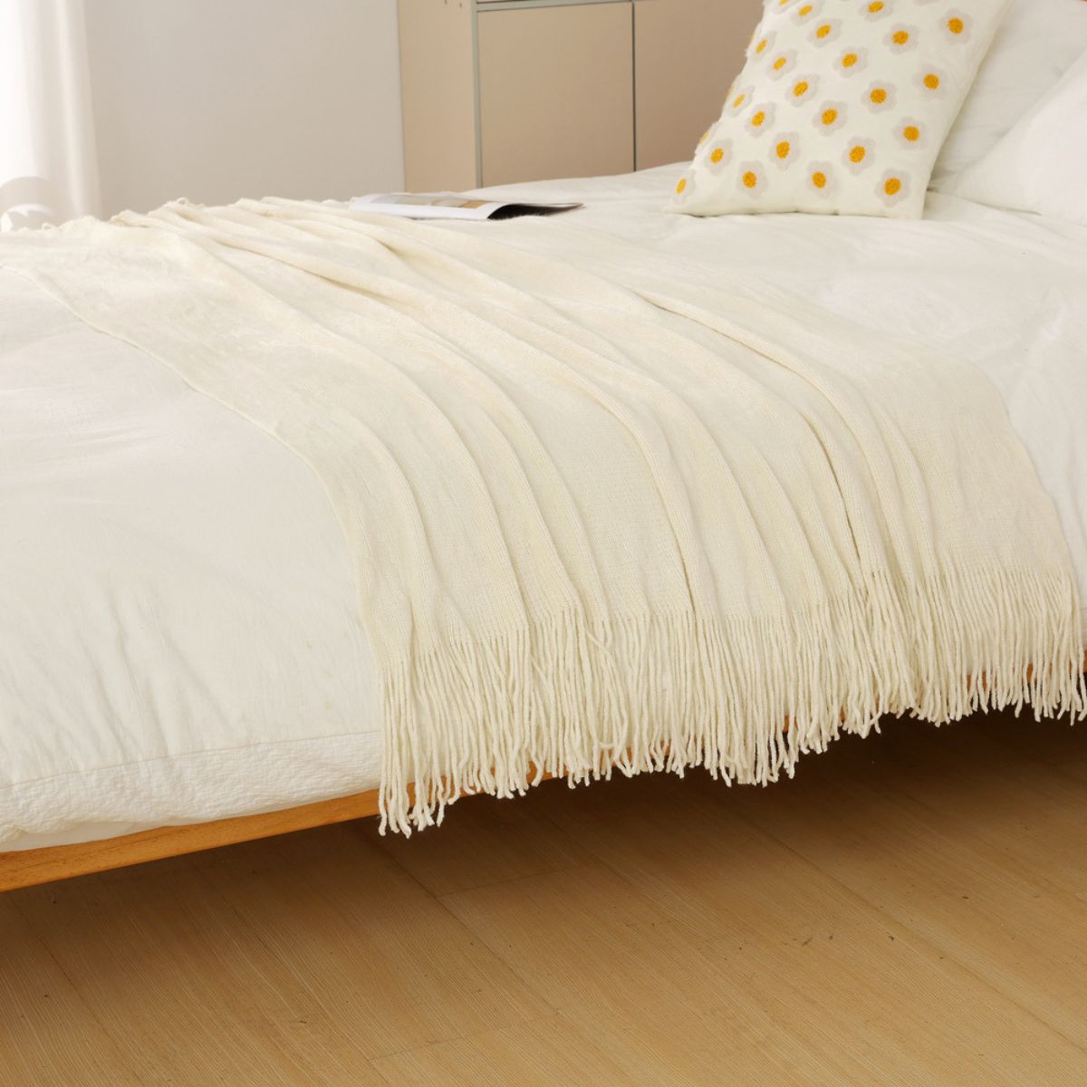 Cream knitted blanket with tassels displayed on bed with pillow