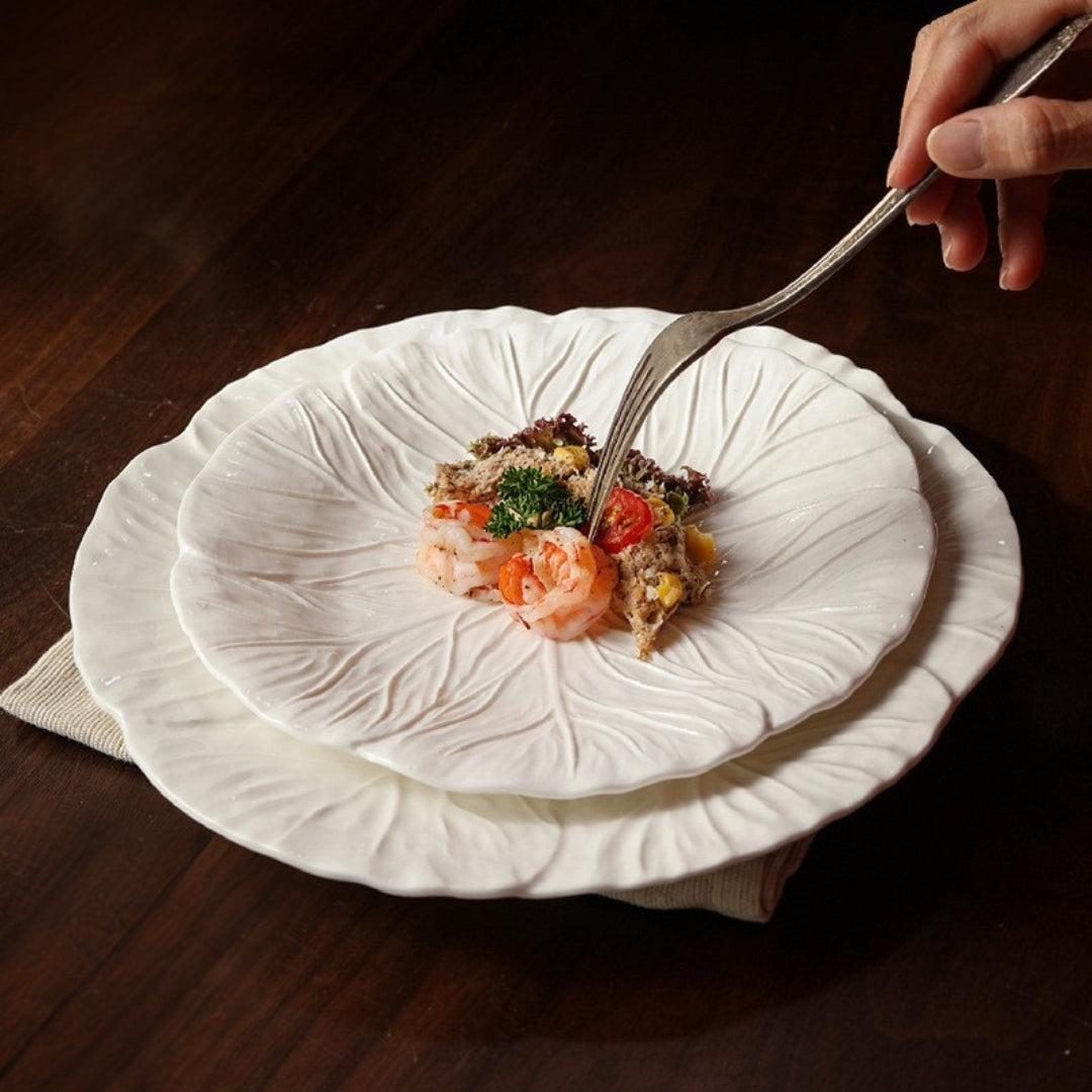 Hand using fork on ceramic leaf plate with food, cozy dining setting