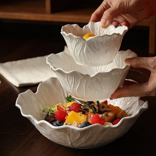 Hands arranging layered ceramic bowls over salad, rustic style