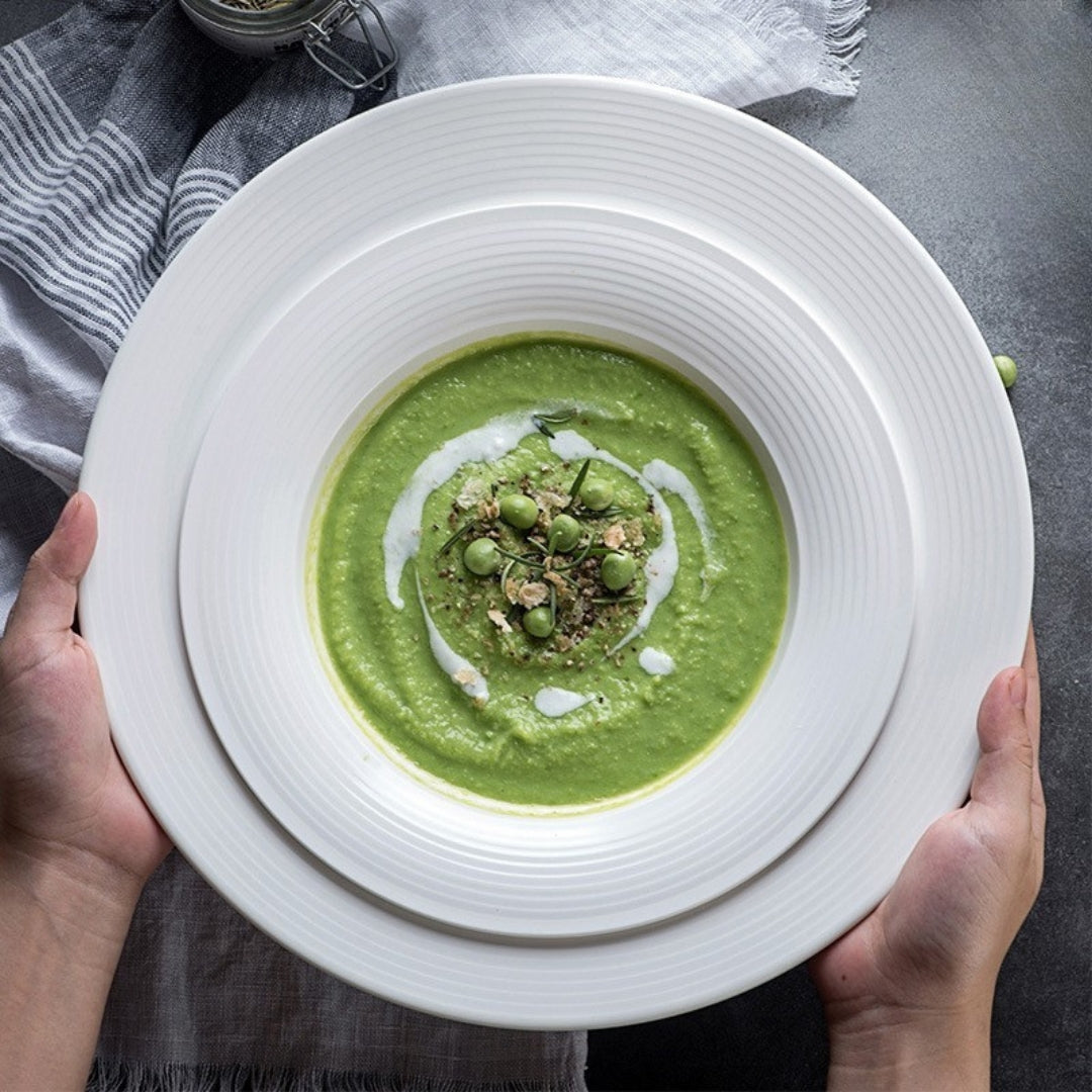Hands holding white textured plate with green pea soup, cozy mealtime moment