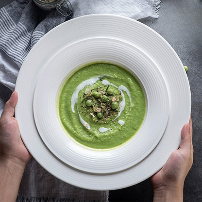 Hands holding white textured plate with green pea soup, cozy mealtime moment