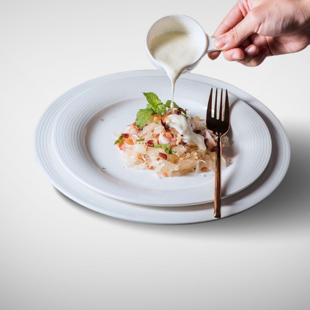 Cream being poured onto salad on white ceramic plate, with golden fork