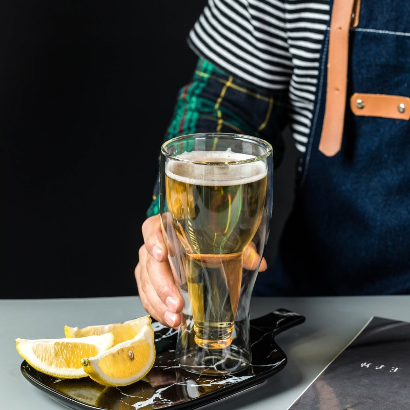 A person's hand holding a double-wall glass, showcasing the unique design and the golden color of the beer inside.