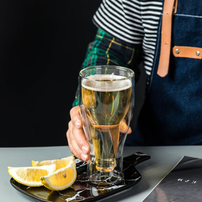A person's hand holding a double-wall glass, showcasing the unique design and the golden color of the beer inside.