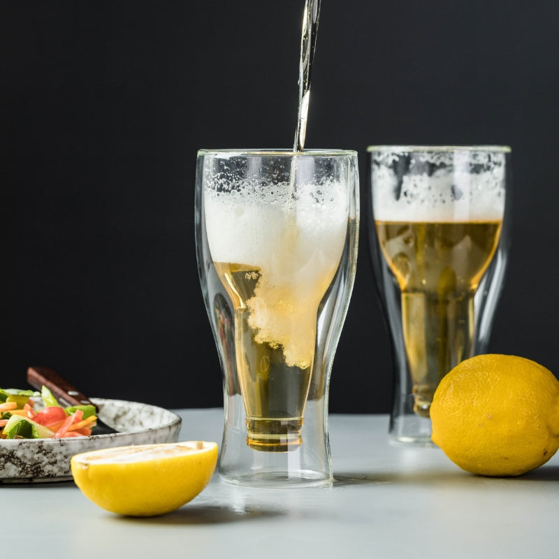 A creative product shot showing beer being poured into the double-wall glass, with foam forming at the top. Another glass is visible in the background.