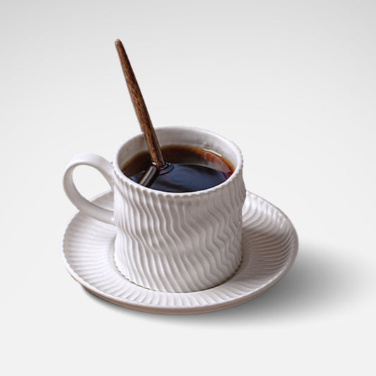 White ripple-textured ceramic coffee cup and saucer set, styled on wooden tray.