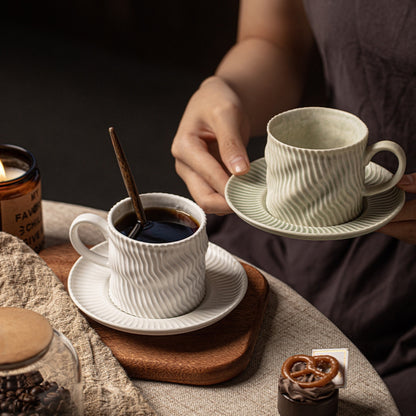 Side view of white ripple-pattern coffee mug with saucer on neutral background.
