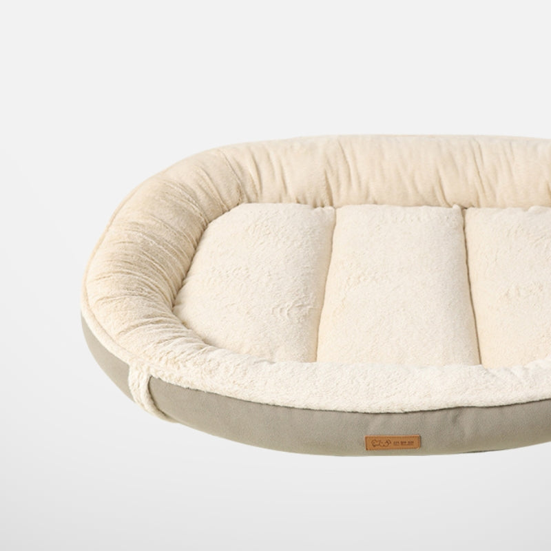 A close-up side view of a plush, oval-shaped dog bed with soft beige fleece and a gray bottom, highlighting the texture and quality of the material.