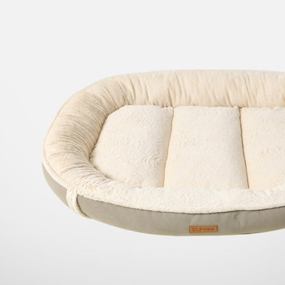 A close-up side view of a plush, oval-shaped dog bed with soft beige fleece and a gray bottom, highlighting the texture and quality of the material.