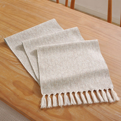 Folded woven table runner with tassel fringe on wood table
