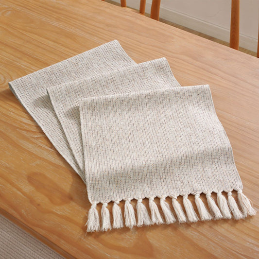 Folded woven table runner with tassel fringe on wood table